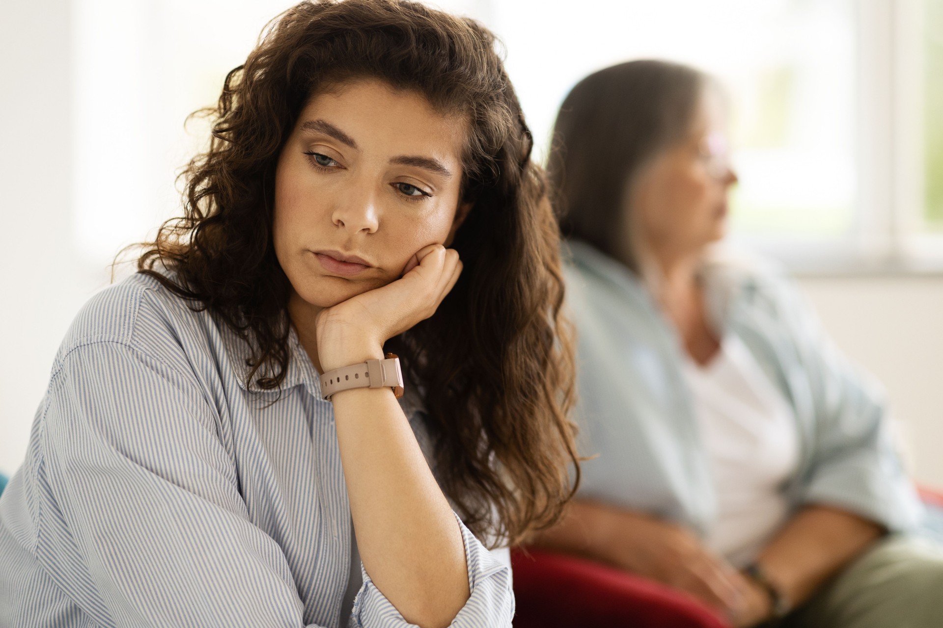 Sad adult caucasian woman ignoring unhappy angry older lady after quarrel in living room