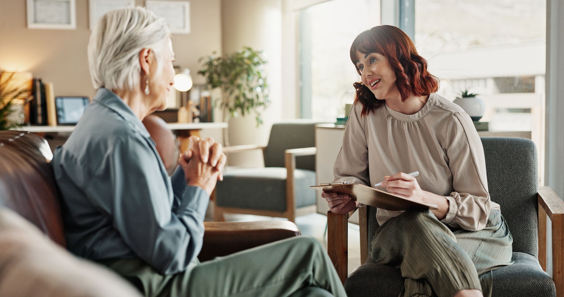 Psychologist, chat and senior woman with notes and smile from mental health assessment in consultation. Writing, support and care with counseling, psychology and evaluation with advice in office